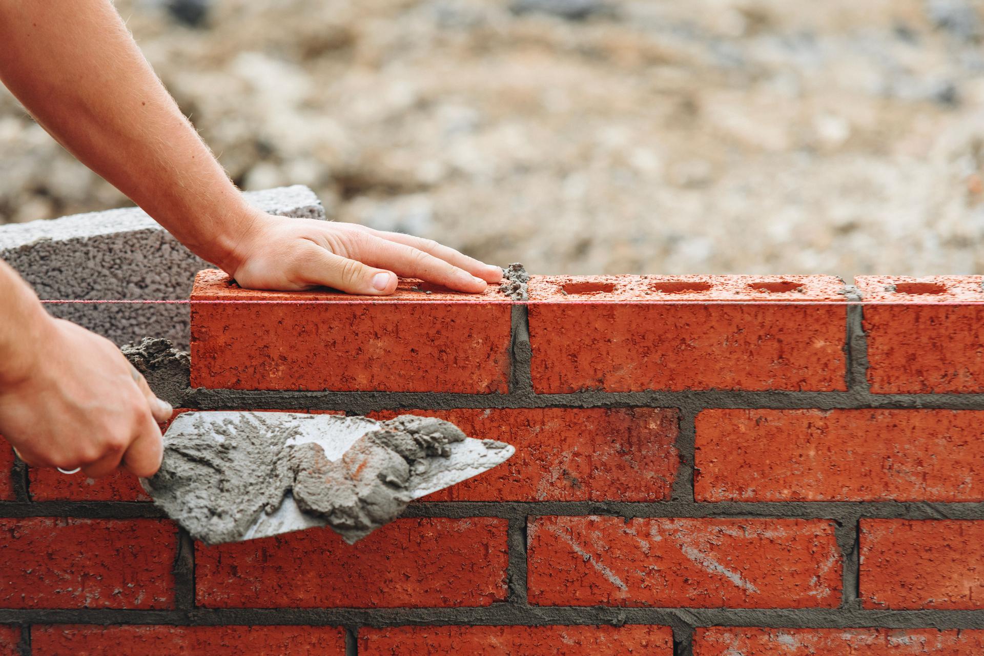 Close-up of skilled bricklayer working on construction site laying bricks for wall construction