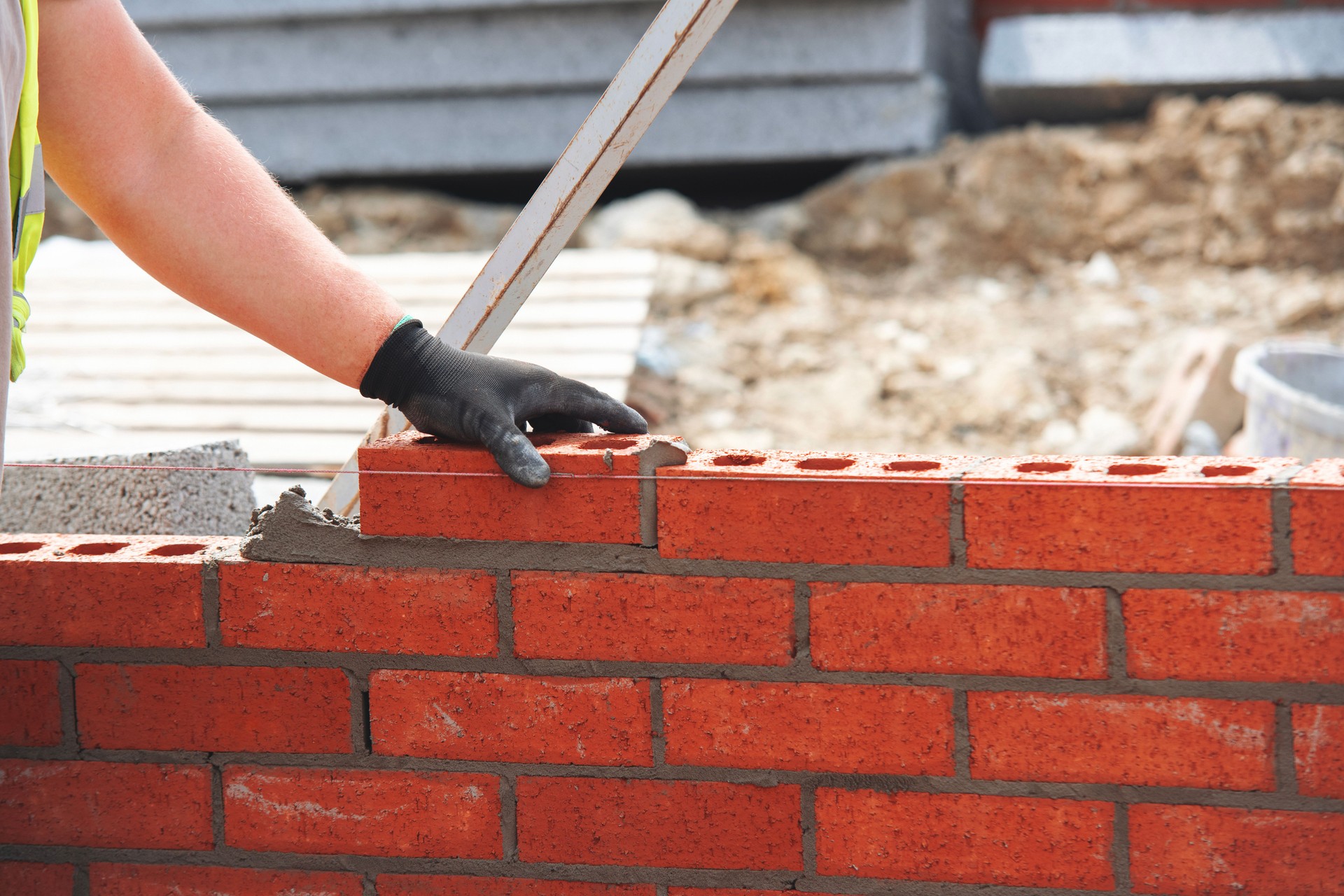 Close-up of skilled bricklayer working on construction site laying red bricks for wall construction